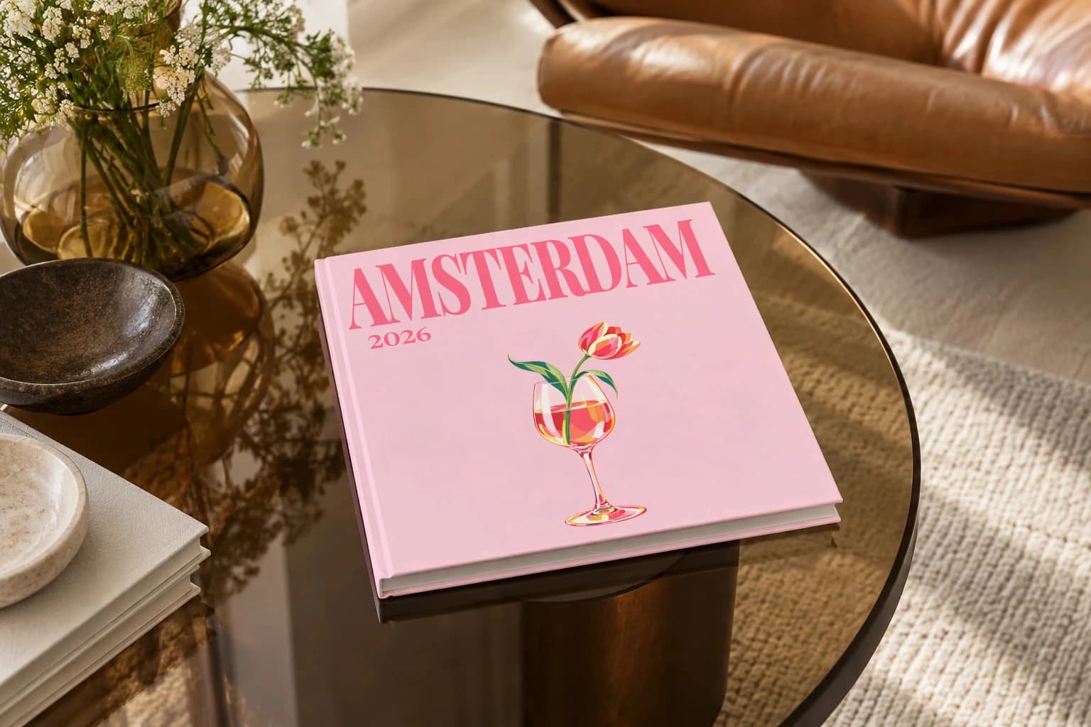 Amsterdam square hardcover photo book with the illustrated cover of the tulip in wine glass, on a smoked glass coffee table beside a leather armchair in warm afternoon light