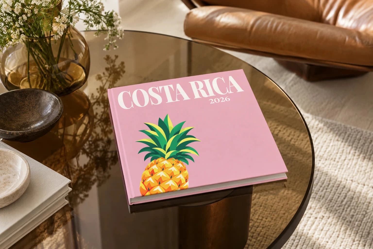 Costa Rica square hardcover photo book with the illustrated cover of the pineapple, on a smoked glass coffee table beside a leather armchair in warm afternoon light
