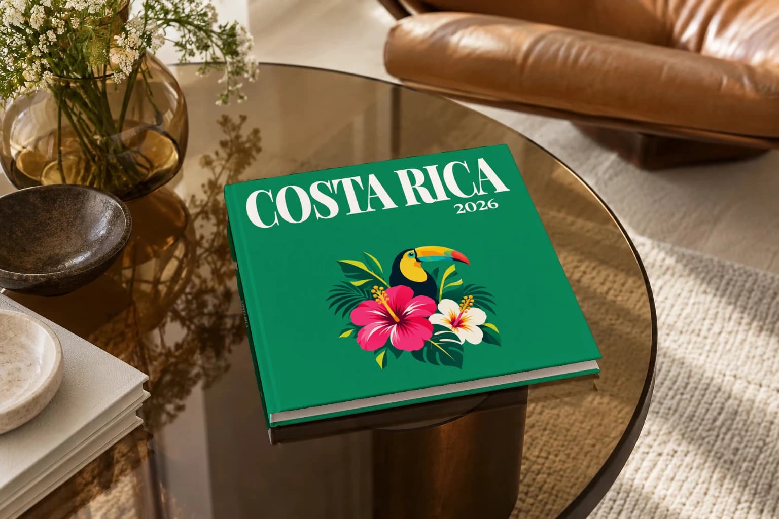 Costa Rica square hardcover photo book with the illustrated cover of the toucan and hibiscus, on a smoked glass coffee table beside a leather armchair in warm afternoon light