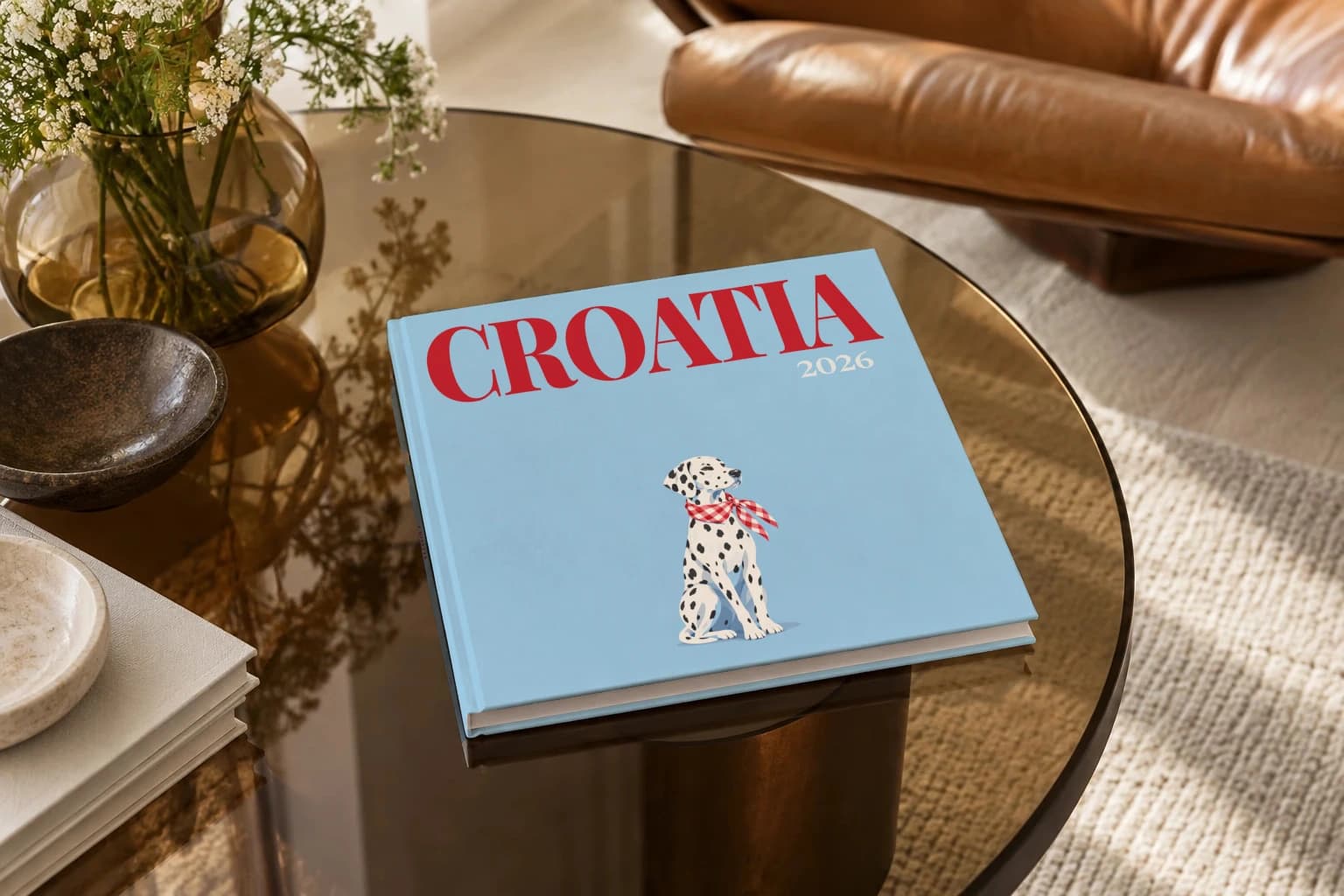 Croatia square hardcover photo book with the illustrated cover of the dalmatian, on a smoked glass coffee table beside a leather armchair in warm afternoon light