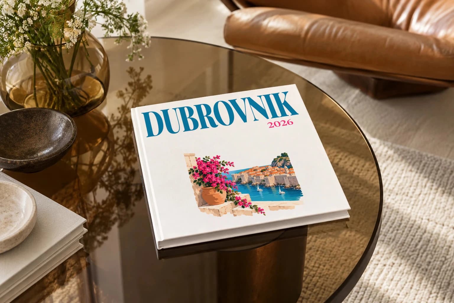 Dubrovnik square hardcover photo book with the illustrated cover of the Dubrovnik and bougainvillea, on a smoked glass coffee table beside a leather armchair in warm afternoon light