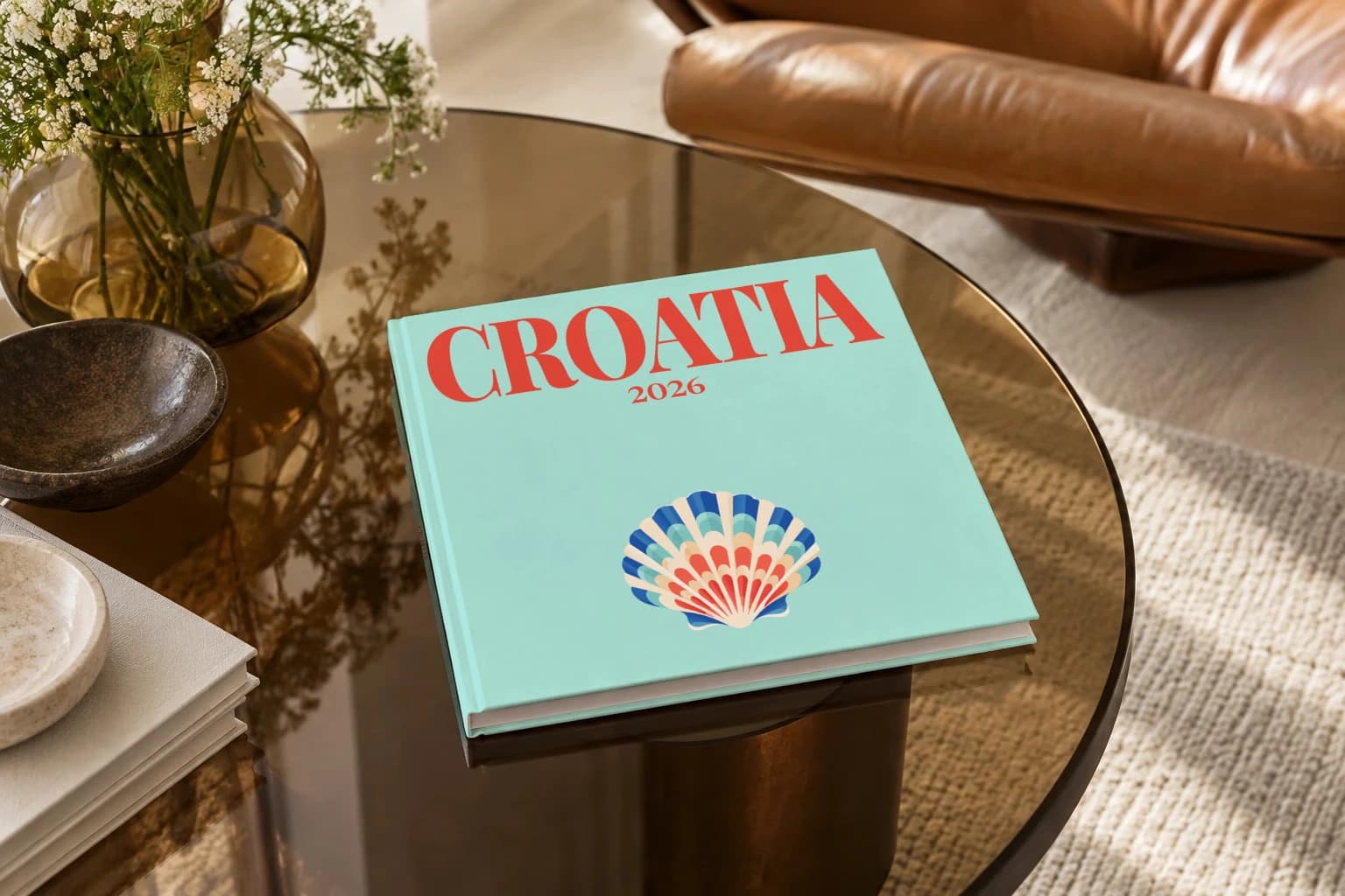 Croatia square hardcover photo book with the illustrated cover of the shell, on a smoked glass coffee table beside a leather armchair in warm afternoon light