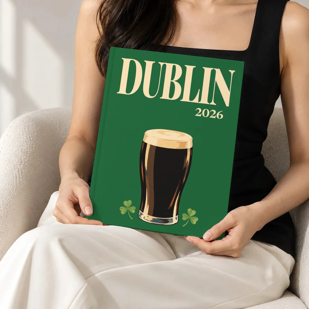 Dublin hardcover photo book with the illustrated cover of the pint of stout, held upright in two hands by a woman in a black top, sitting in a cream boucle armchair