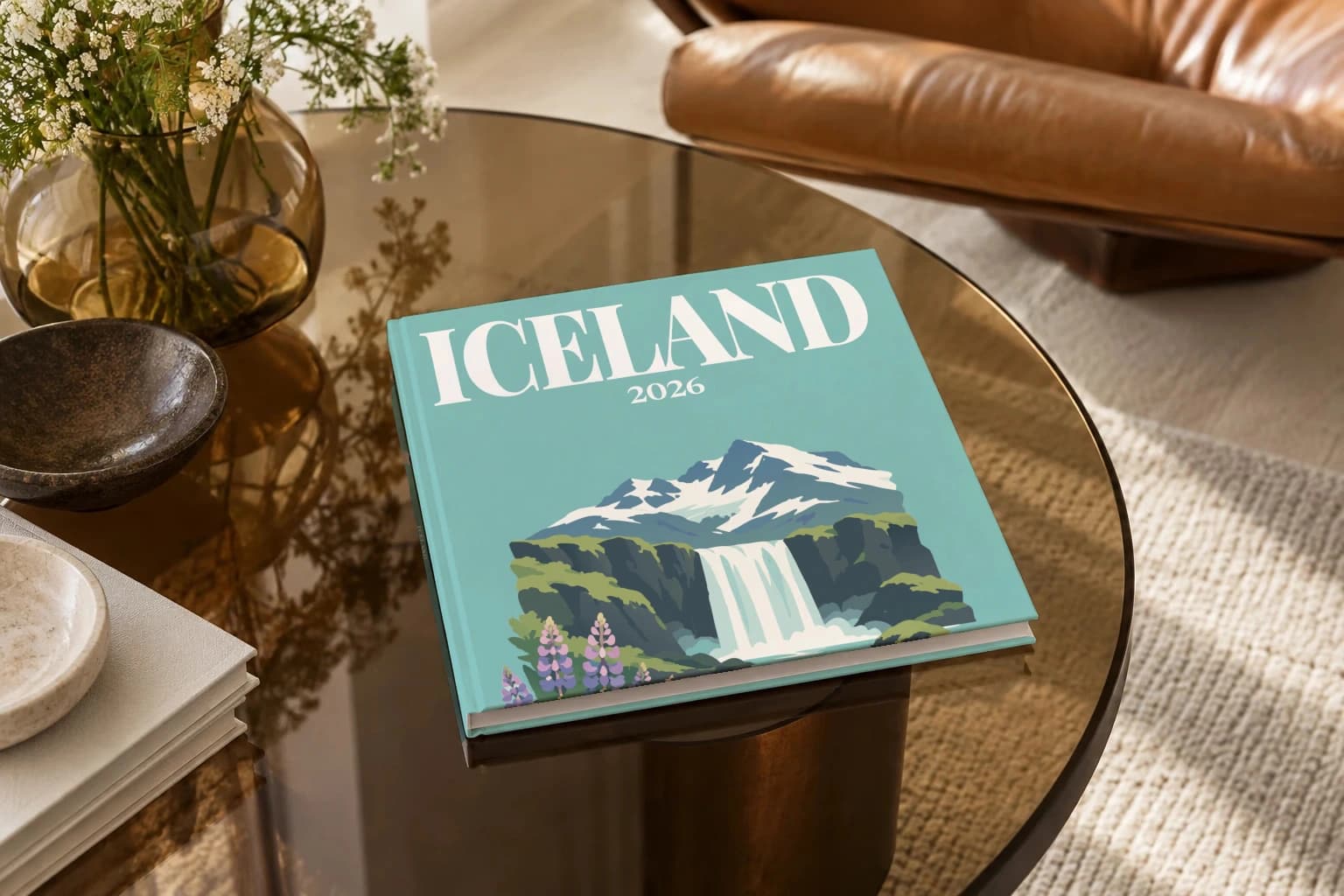 Iceland square hardcover photo book with the illustrated cover of the waterfall and lupins, on a smoked glass coffee table beside a leather armchair in warm afternoon light