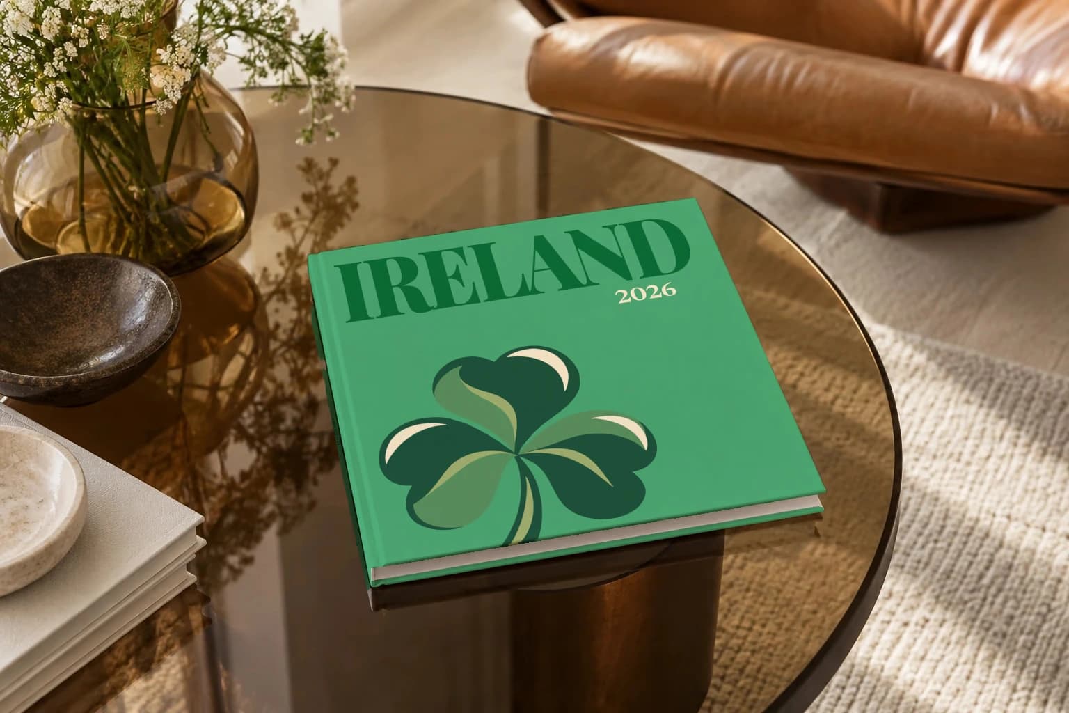 Ireland square hardcover photo book with the illustrated cover of a green shamrock on green, on a smoked glass coffee table beside a leather armchair in warm afternoon light