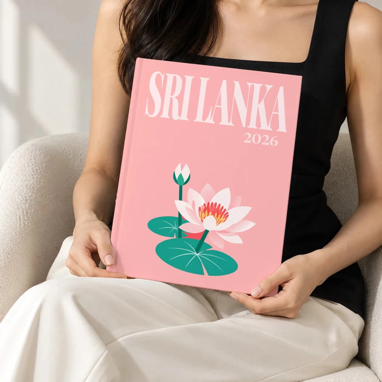 Sri Lanka hardcover photo book with the illustrated cover of the lotus, held upright in two hands by a woman in a black top, sitting in a cream boucle armchair