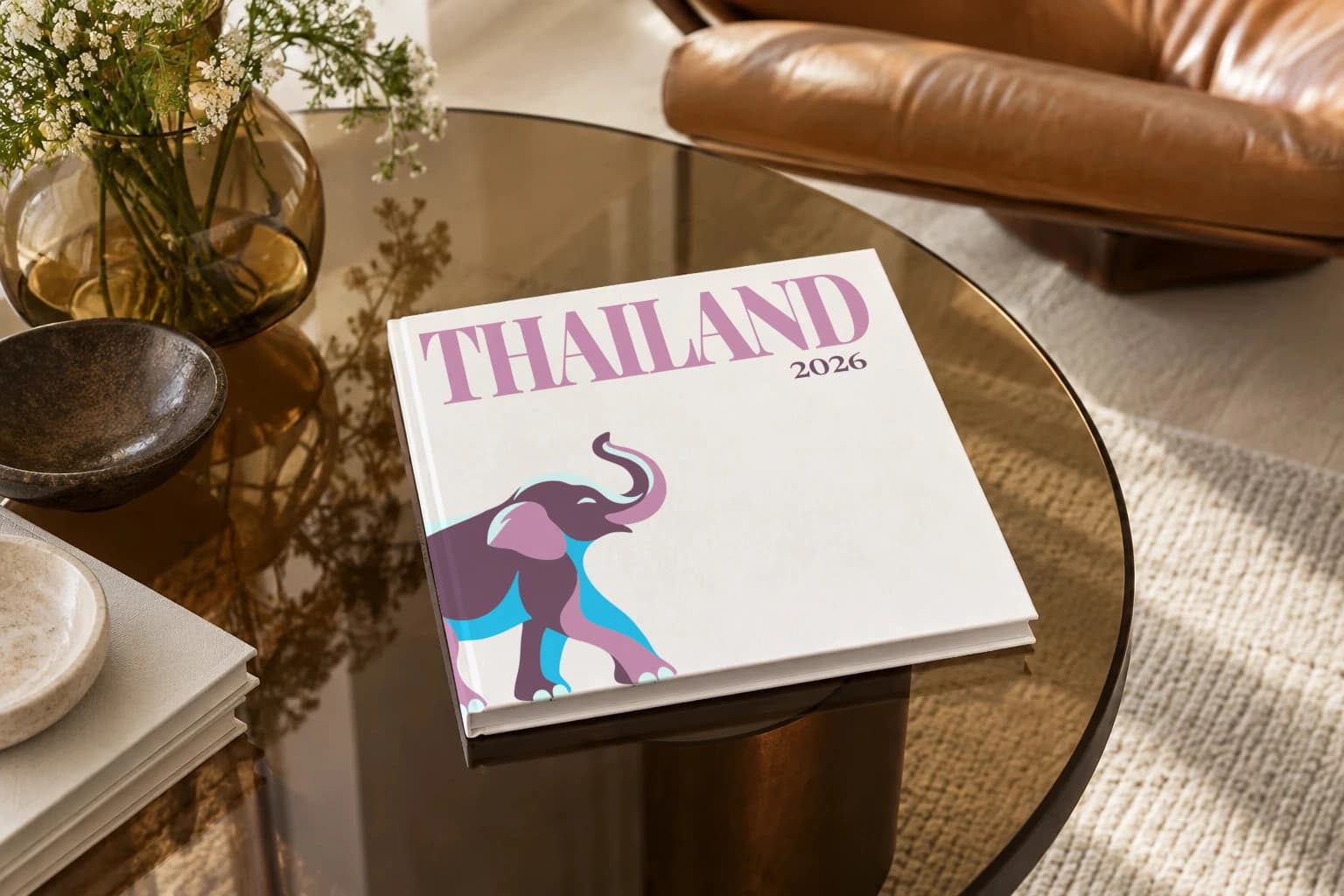 Thailand square hardcover photo book with the illustrated cover of an elephant on white, on a smoked glass coffee table beside a leather armchair in warm afternoon light
