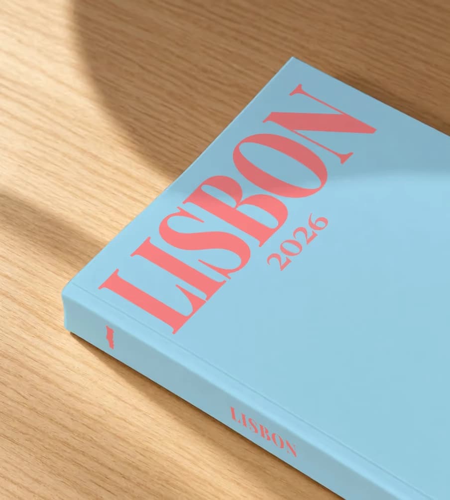 Lisbon softcover photo book with an illustrated cover of a sardine painted like azulejo tiles, lying on an oak desk in dappled afternoon sunlight