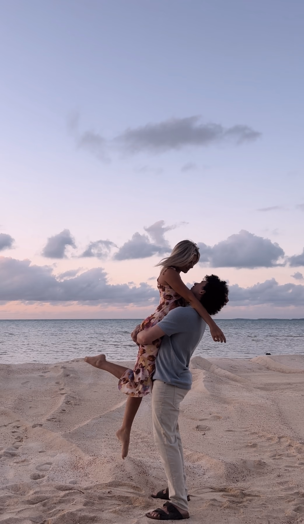 Couple embracing on a beach beneath a pastel evening sky