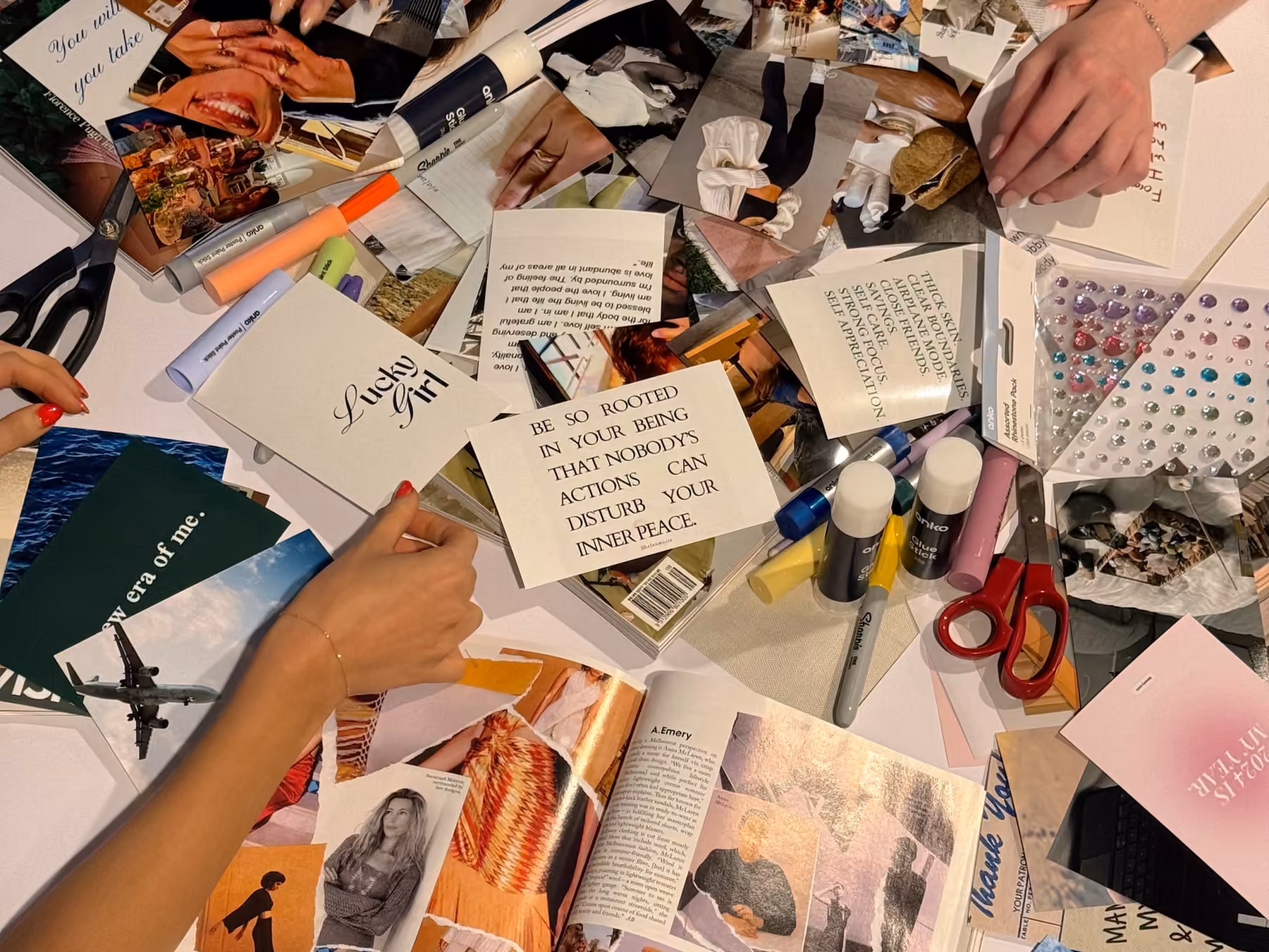 Friends making a travel scrapbook together at a table with printed photos, magazine cutouts, glue sticks and scissors