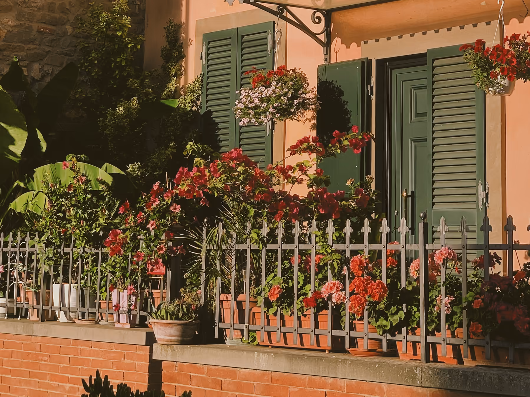 Sunlit Italian village house with green shutters and red geraniums, the kind of place that appears in a family's old travel photos