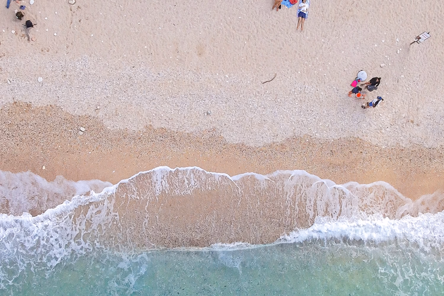 Overhead view of beachgoers and waves meeting turquoise water