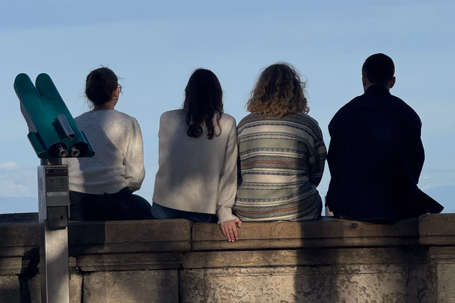 Four people sitting together at a viewpoint beneath a blue sky