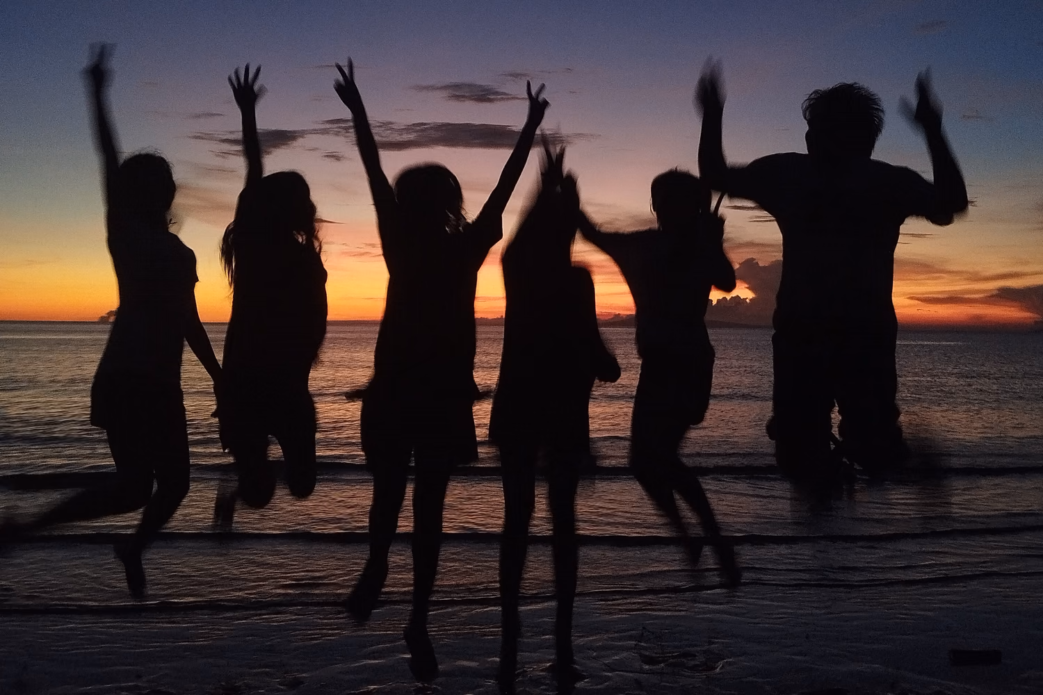 Friends jumping beside the sea at sunset