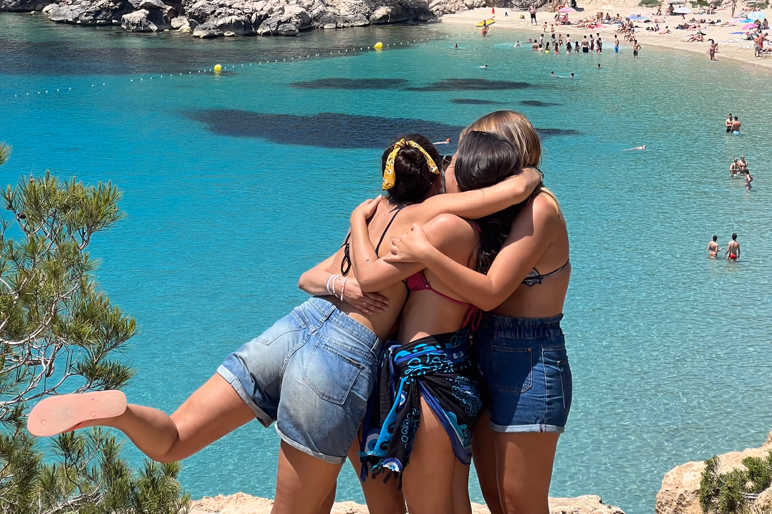 Three friends embracing above a turquoise bay