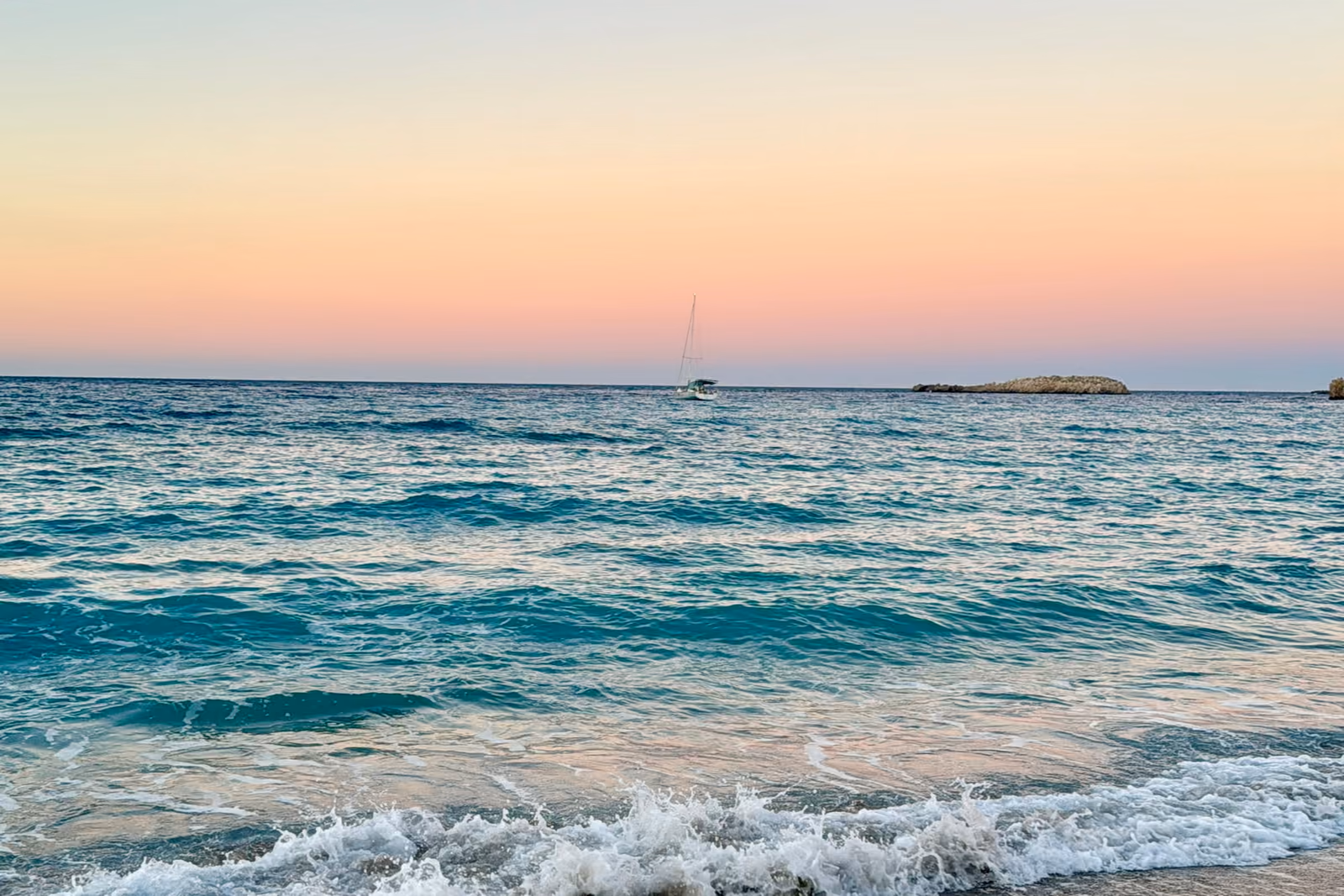 Gentle waves reaching a sandy beach beneath a pink evening sky