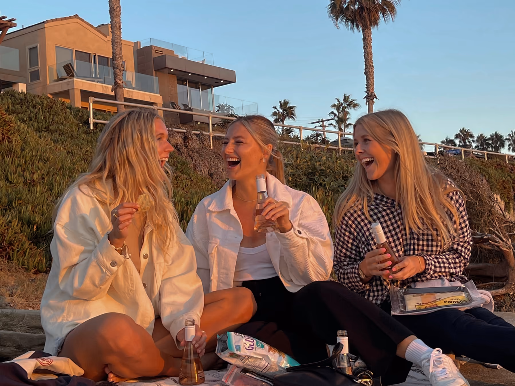 Three exchange students laughing together at a sunset picnic under palm trees during their semester abroad