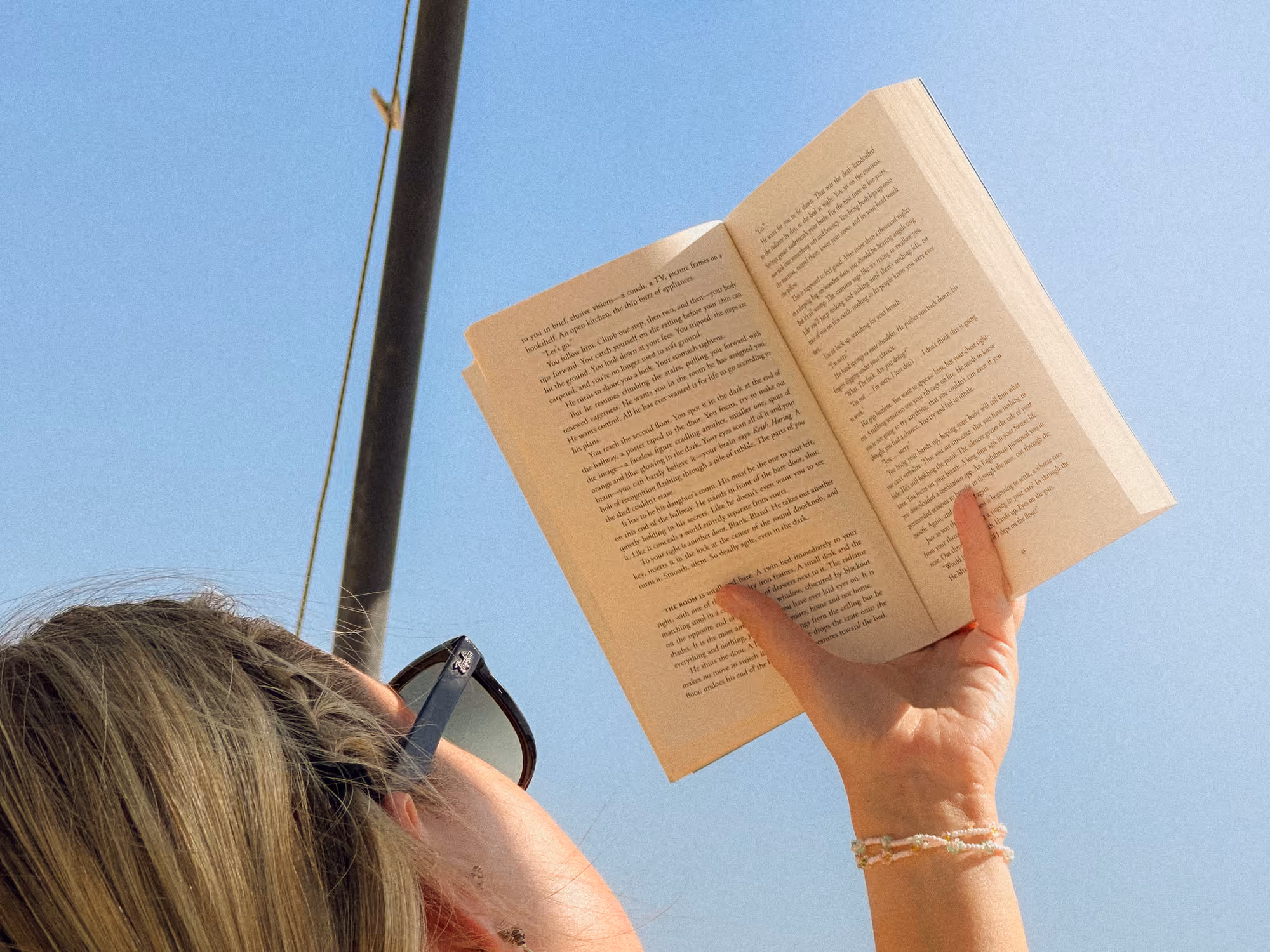 Student reading a paperback under a beach umbrella on a sunny afternoon during a semester abroad