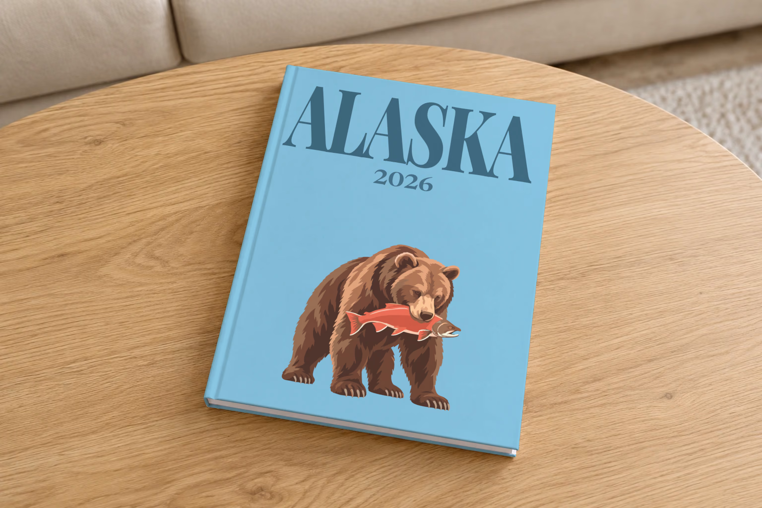 Alaska hardcover photo book with the illustrated cover of a grizzly bear catching a salmon on blue, on a round oak coffee table in a bright living room