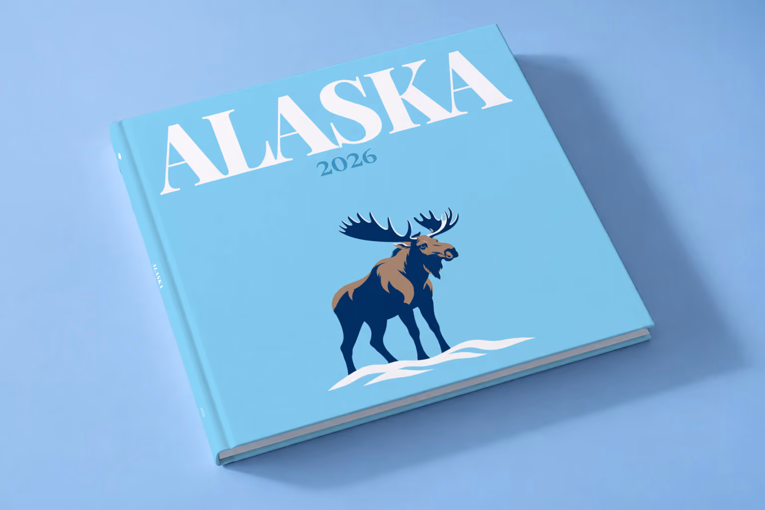 Alaska square hardcover photo book with the illustrated cover of a navy moose in the snow on sky blue, lying on a pale blue studio backdrop
