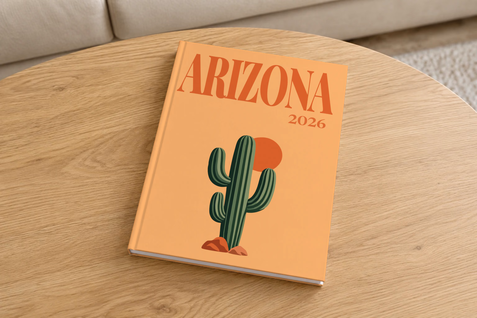 Arizona hardcover photo book with the illustrated cover of a saguaro cactus and a setting sun on apricot, on a round oak coffee table in a bright living room