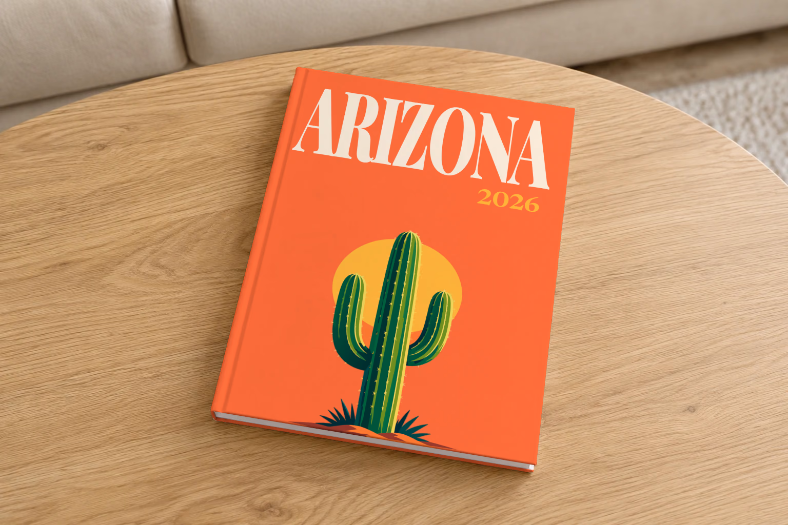 Arizona hardcover photo book with the illustrated cover of a saguaro cactus against a yellow sun on orange, on a round oak coffee table in a bright living room
