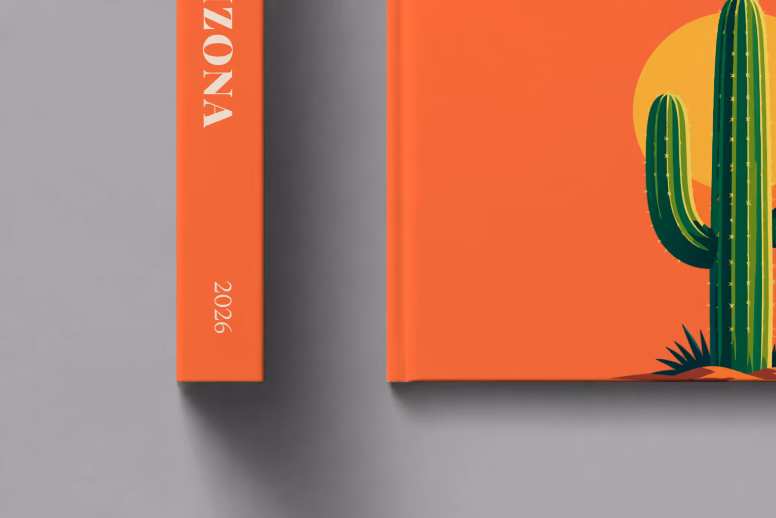 Arizona hardcover photo book with the illustrated cover of a saguaro cactus against a yellow sun on orange, shown close up beside its spine on a pale grey studio surface
