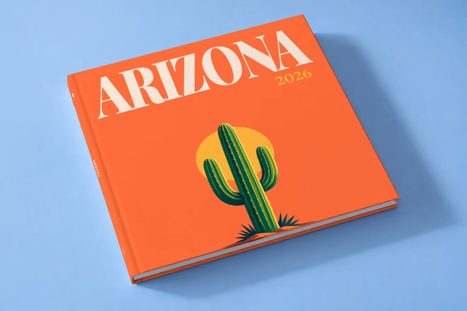 Arizona square hardcover photo book with the illustrated cover of a saguaro cactus against a yellow sun on orange, lying on a pale blue studio backdrop