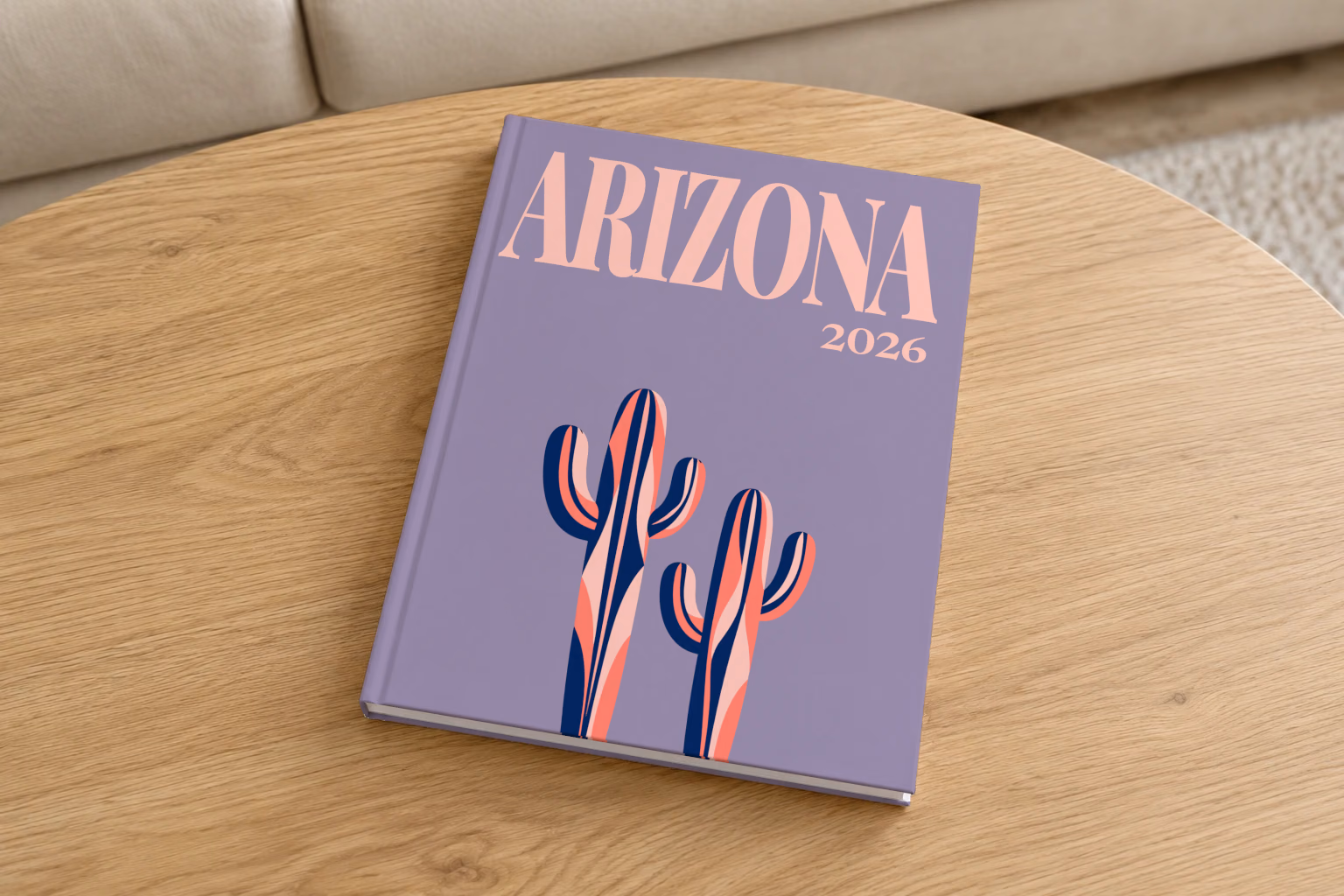 Arizona hardcover photo book with the illustrated cover of two stylised saguaro cacti on dusty purple, on a round oak coffee table in a bright living room