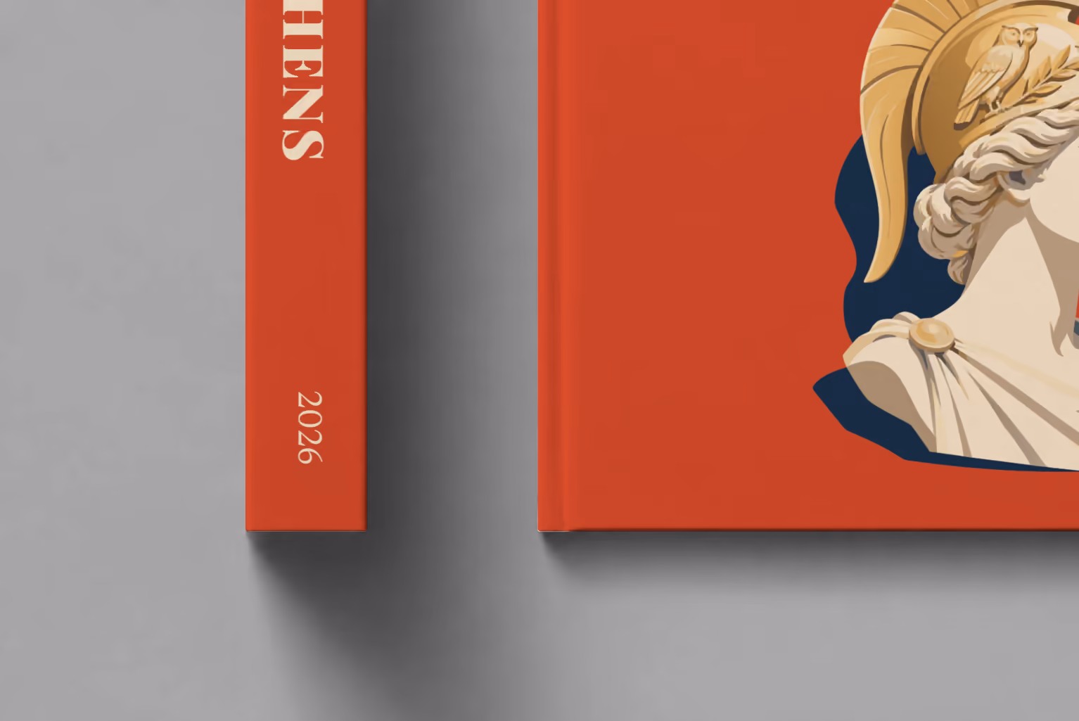 Athens hardcover photo book with the illustrated cover of a bust of Athena in a helmet on red, shown close up beside its spine on a pale grey studio surface