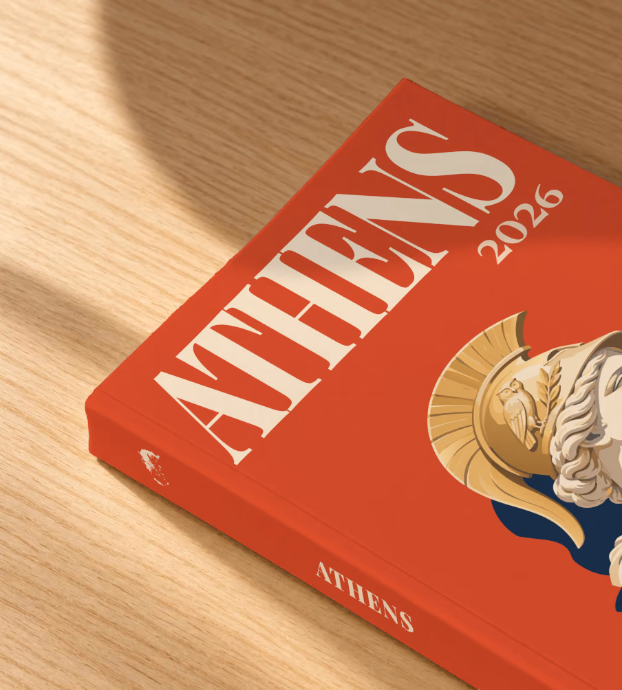 Athens softcover photo book with the illustrated cover of a bust of Athena in a helmet on red, lying on an oak desk in dappled afternoon sunlight