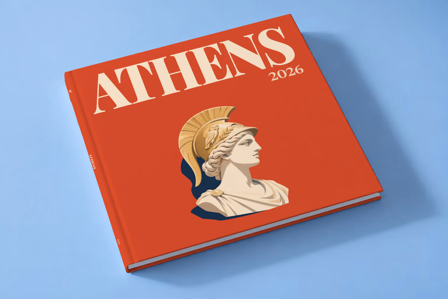Athens square hardcover photo book with the illustrated cover of a bust of Athena in a helmet on red, lying on a pale blue studio backdrop