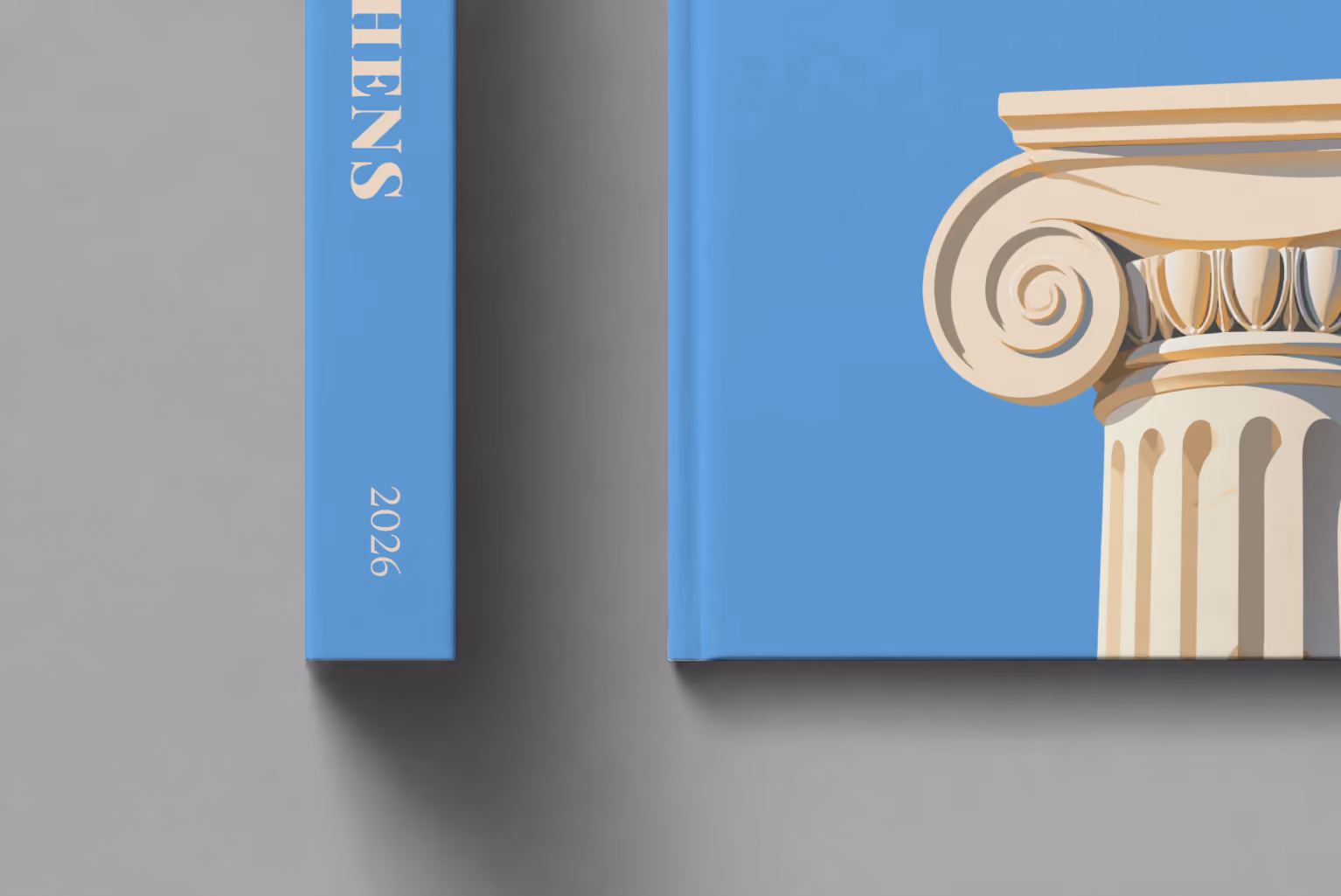 Athens hardcover photo book with the illustrated cover of an Ionic capital on blue, shown close up beside its spine on a pale grey studio surface