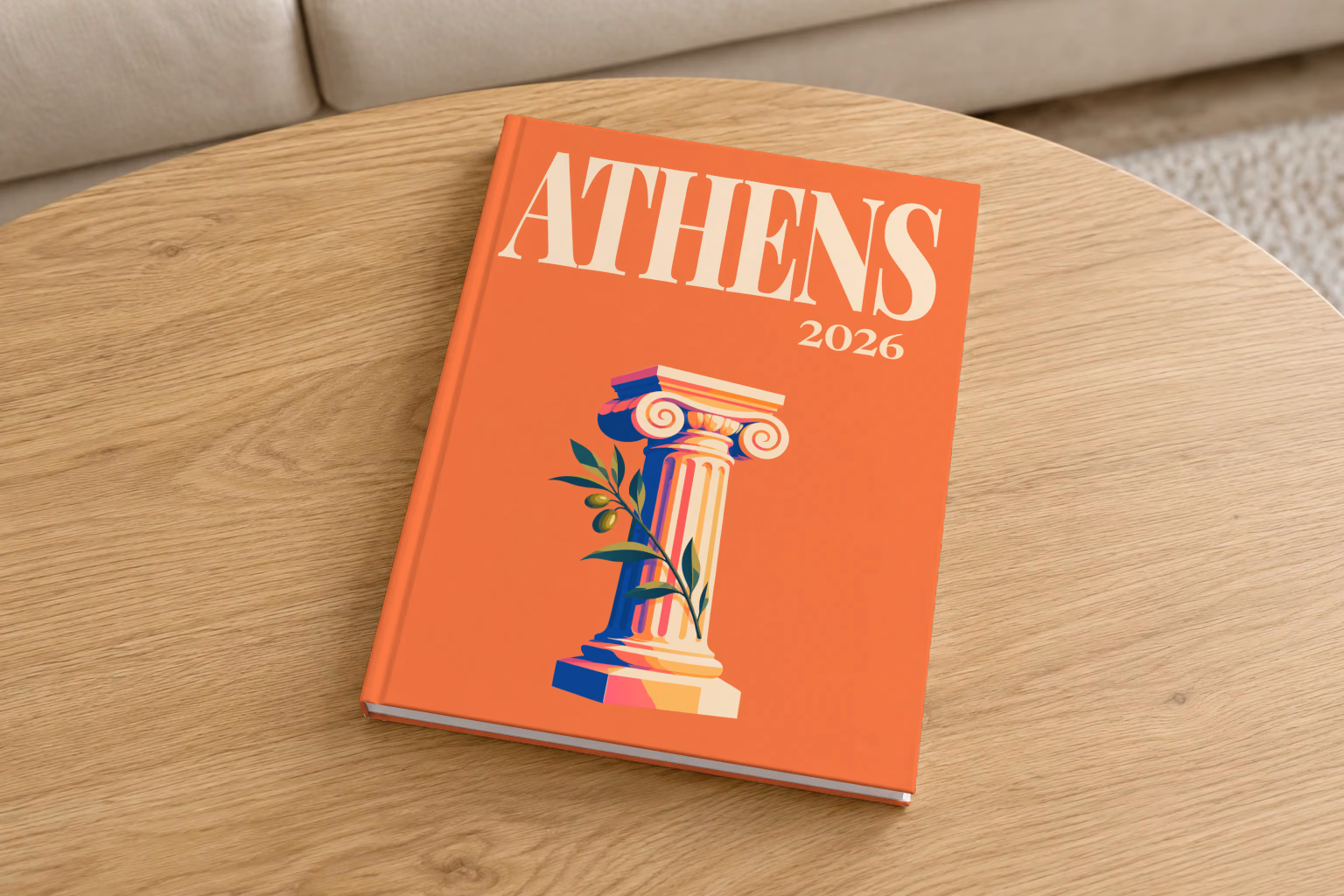 Athens hardcover photo book with the illustrated cover of an Ionic column and an olive sprig on orange, on a round oak coffee table in a bright living room
