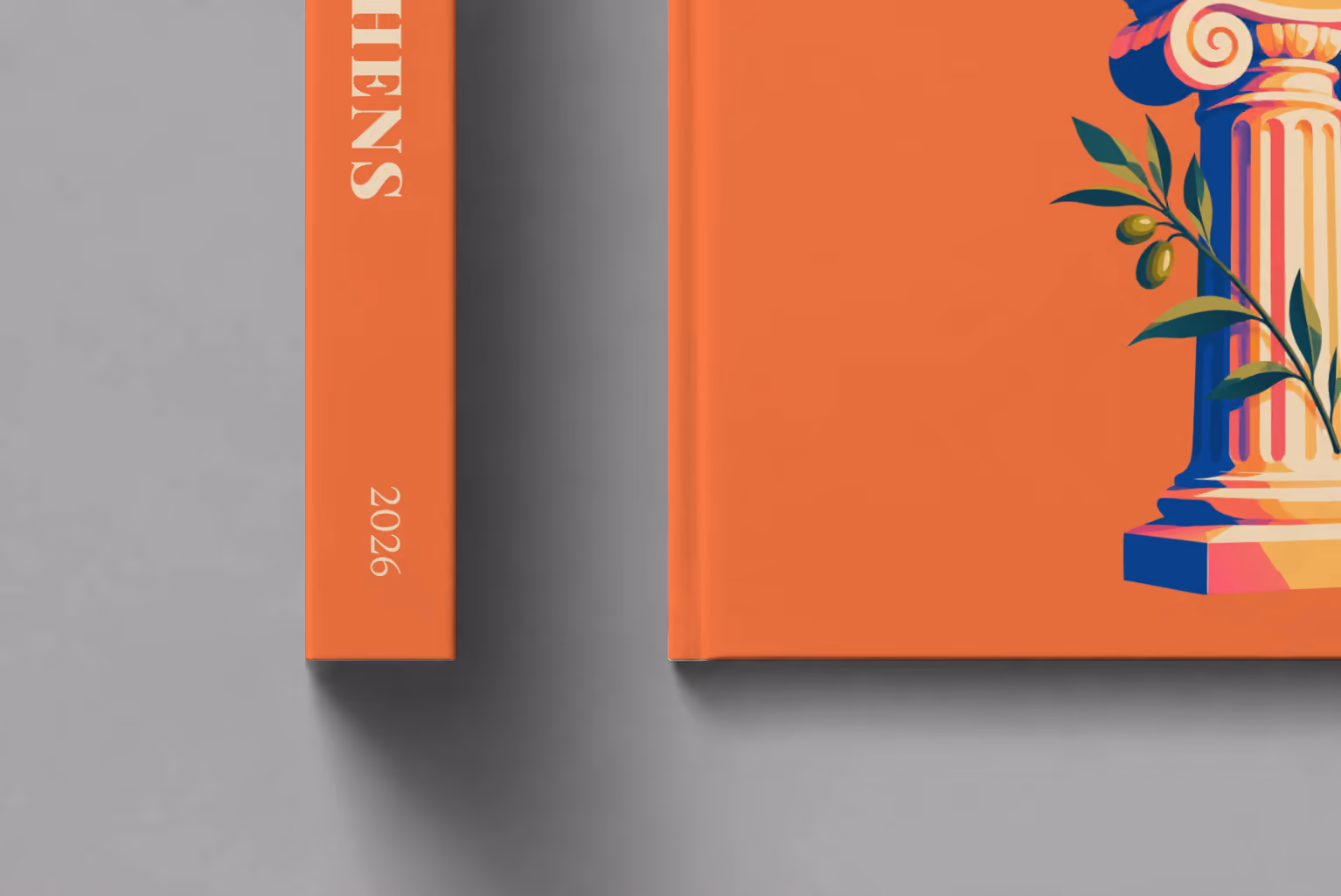 Athens hardcover photo book with the illustrated cover of an Ionic column and an olive sprig on orange, shown close up beside its spine on a pale grey studio surface