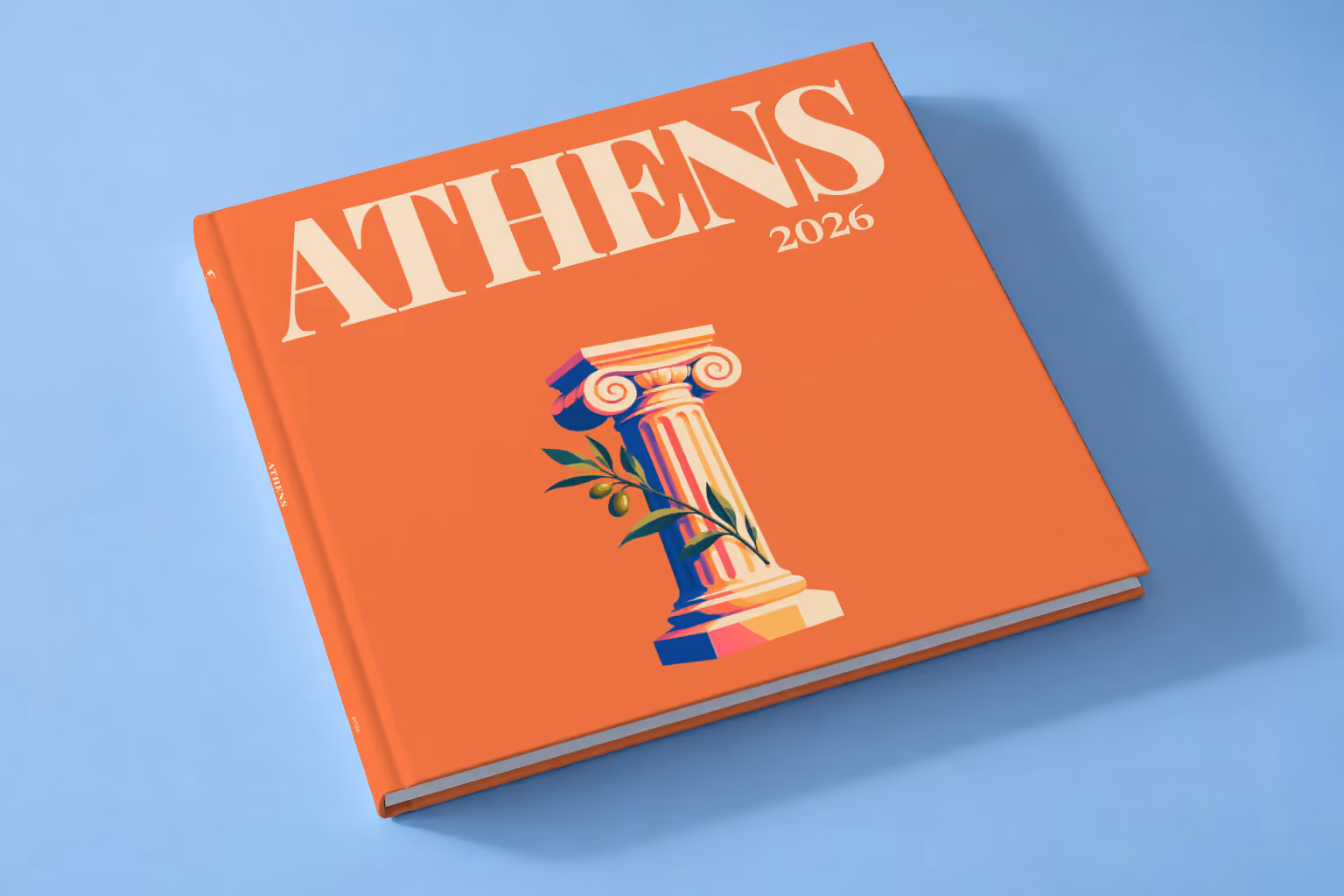 Athens square hardcover photo book with the illustrated cover of an Ionic column and an olive sprig on orange, lying on a pale blue studio backdrop
