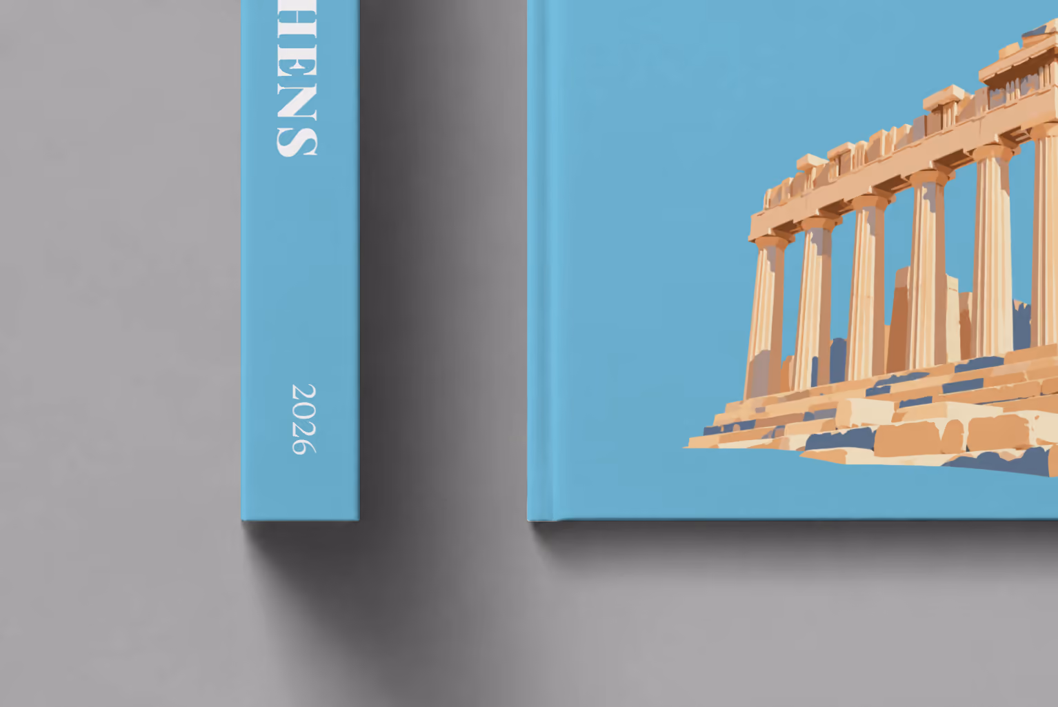 Athens hardcover photo book with the illustrated cover of the Parthenon on blue, shown close up beside its spine on a pale grey studio surface