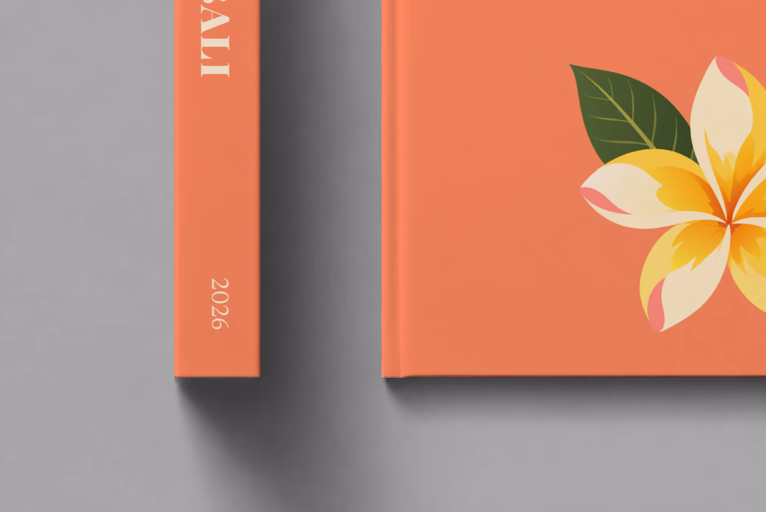 Bali hardcover photo book with the illustrated cover of a yellow frangipani flower on coral, shown close up beside its spine on a pale grey studio surface