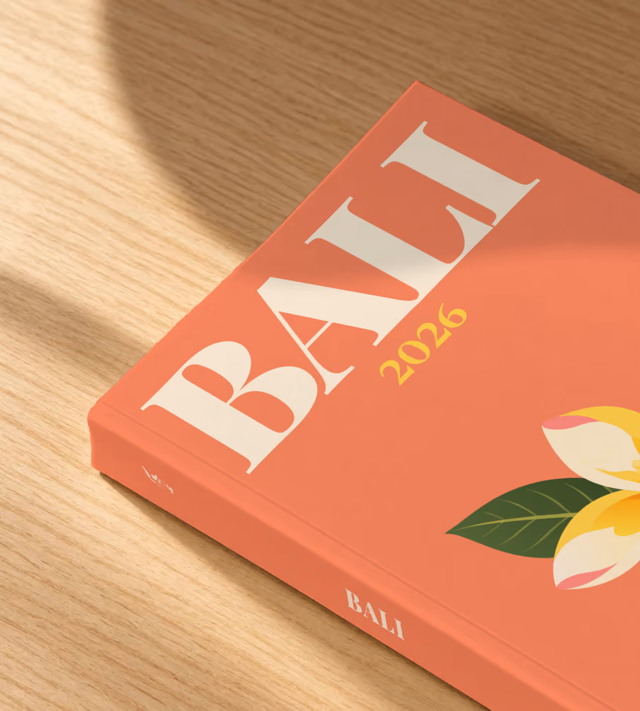 Bali softcover photo book with the illustrated cover of a yellow frangipani flower on coral, lying on an oak desk in dappled afternoon sunlight