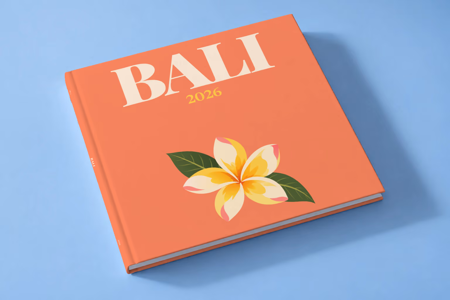 Bali square hardcover photo book with the illustrated cover of a yellow frangipani flower on coral, lying on a pale blue studio backdrop