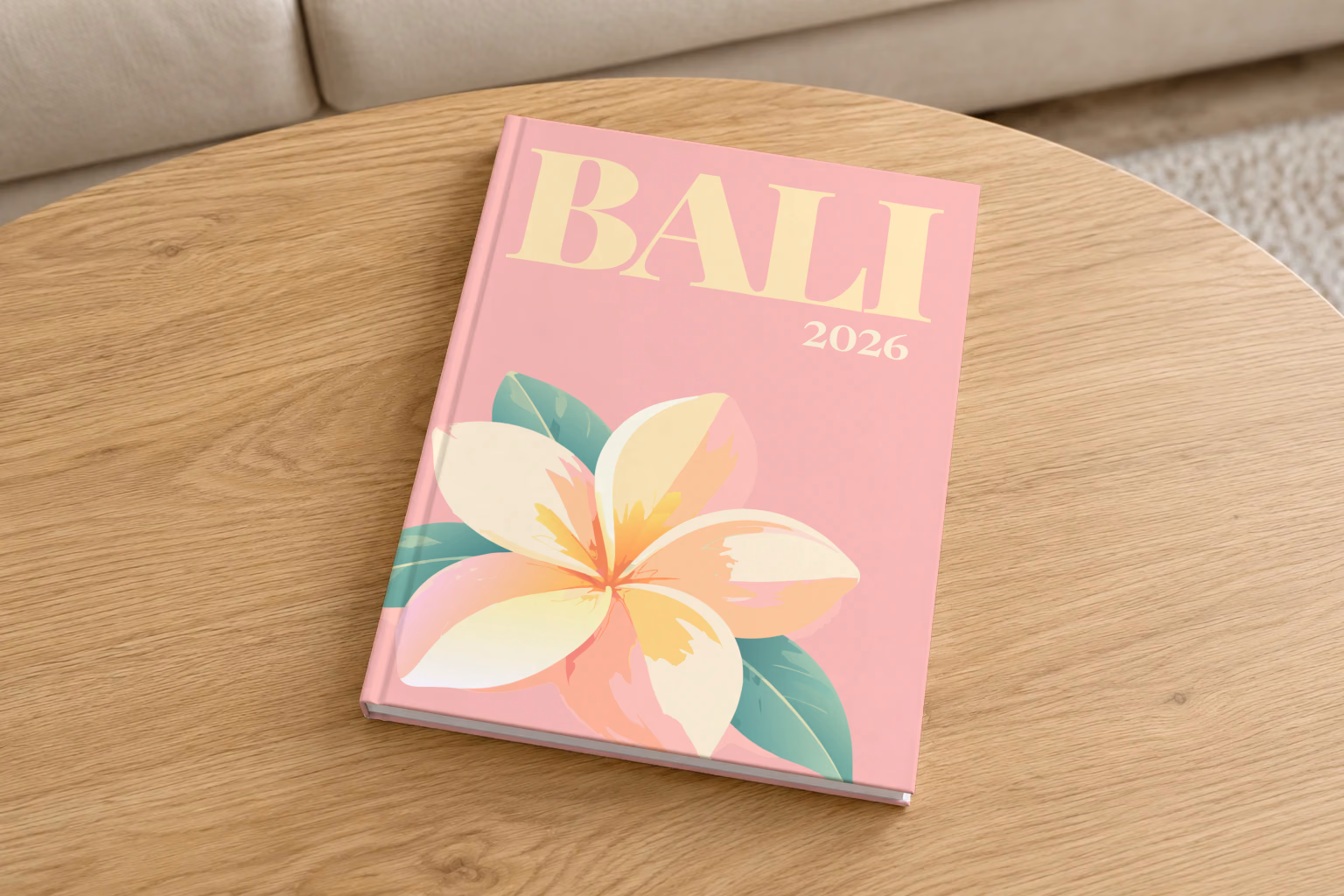 Bali hardcover photo book with the illustrated cover of a white and yellow frangipani flower on pink, on a round oak coffee table in a bright living room