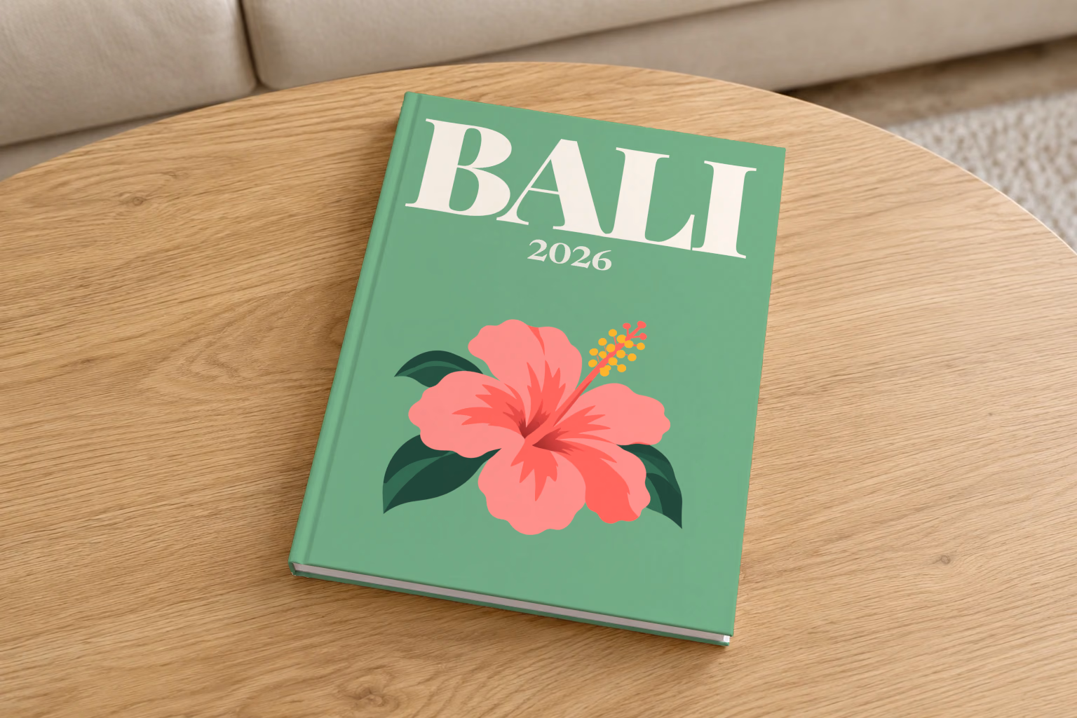 Bali hardcover photo book with the illustrated cover of a pink hibiscus flower on sage green, on a round oak coffee table in a bright living room