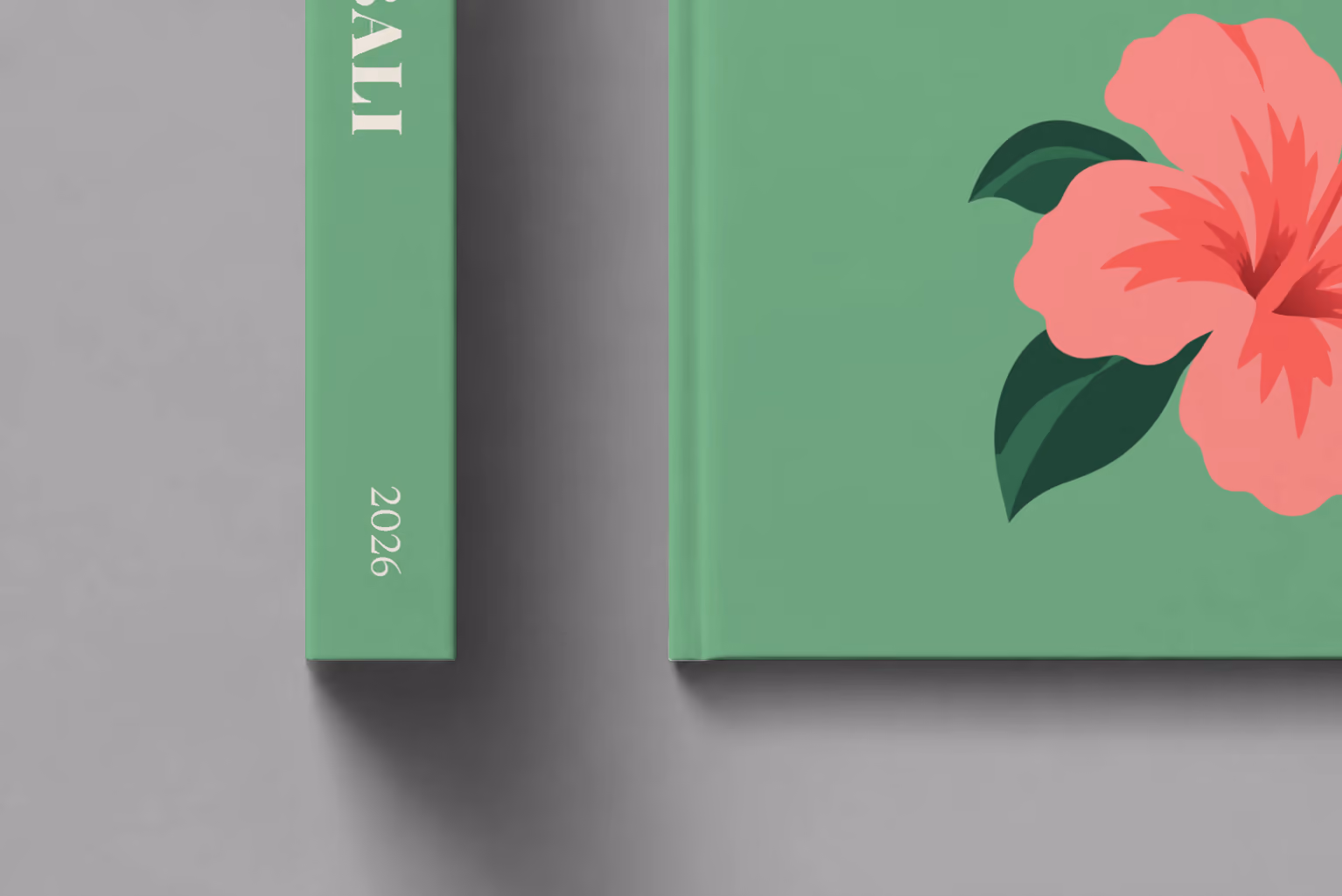 Bali hardcover photo book with the illustrated cover of a pink hibiscus flower on sage green, shown close up beside its spine on a pale grey studio surface