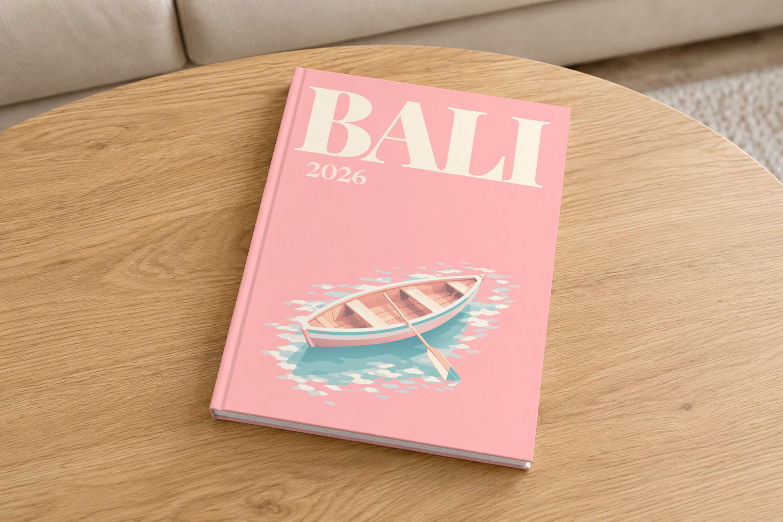 Bali hardcover photo book with the illustrated cover of a wooden rowboat on clear water on pink, on a round oak coffee table in a bright living room