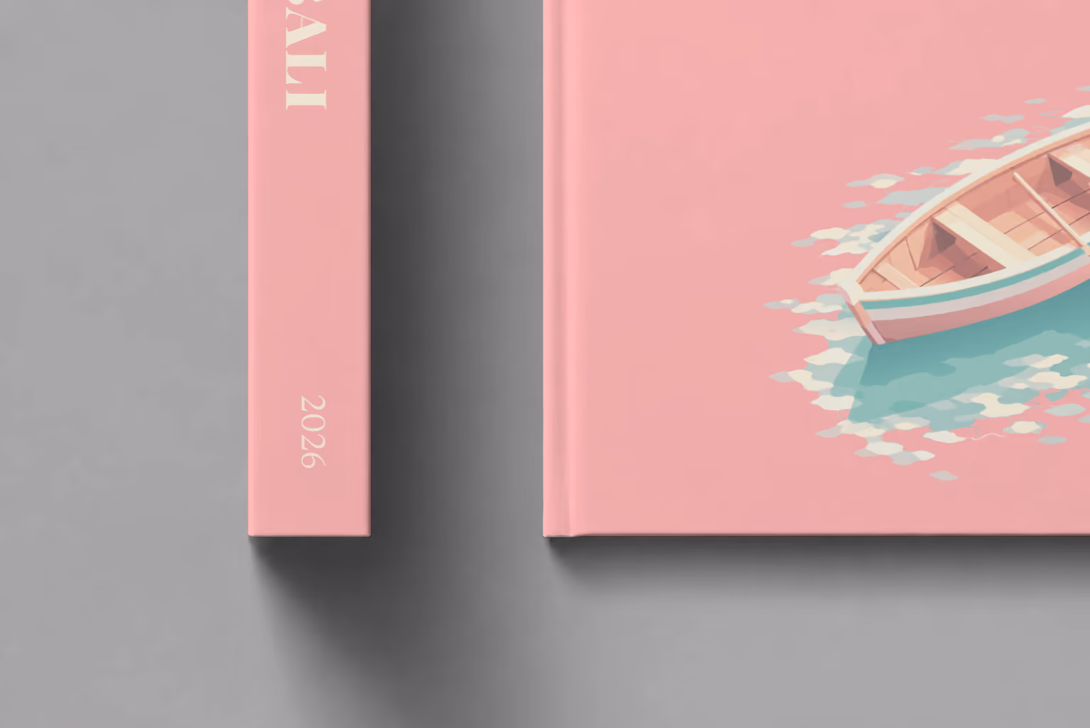 Bali hardcover photo book with the illustrated cover of a wooden rowboat on clear water on pink, shown close up beside its spine on a pale grey studio surface