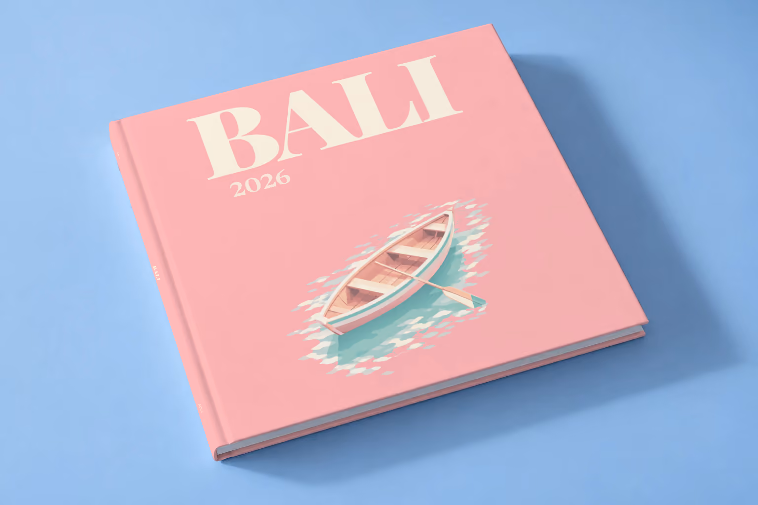 Bali square hardcover photo book with the illustrated cover of a wooden rowboat on clear water on pink, lying on a pale blue studio backdrop