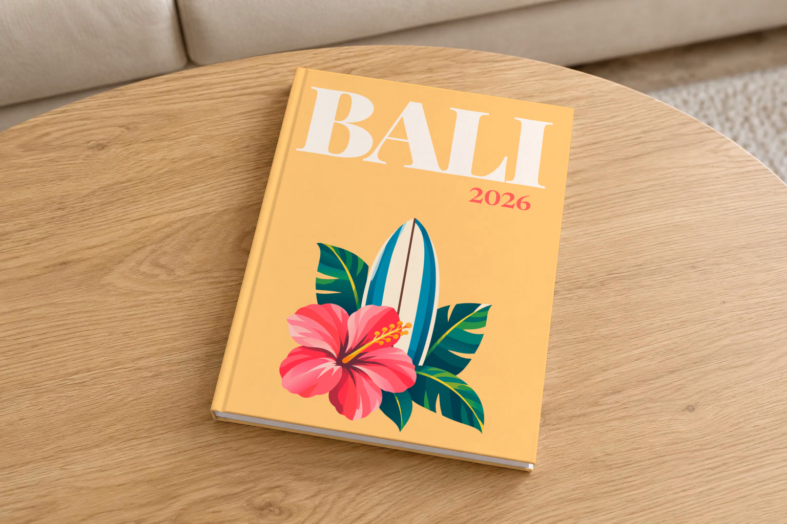 Bali hardcover photo book with the illustrated cover of a surfboard with a pink hibiscus and palm leaves on apricot, on a round oak coffee table in a bright living room