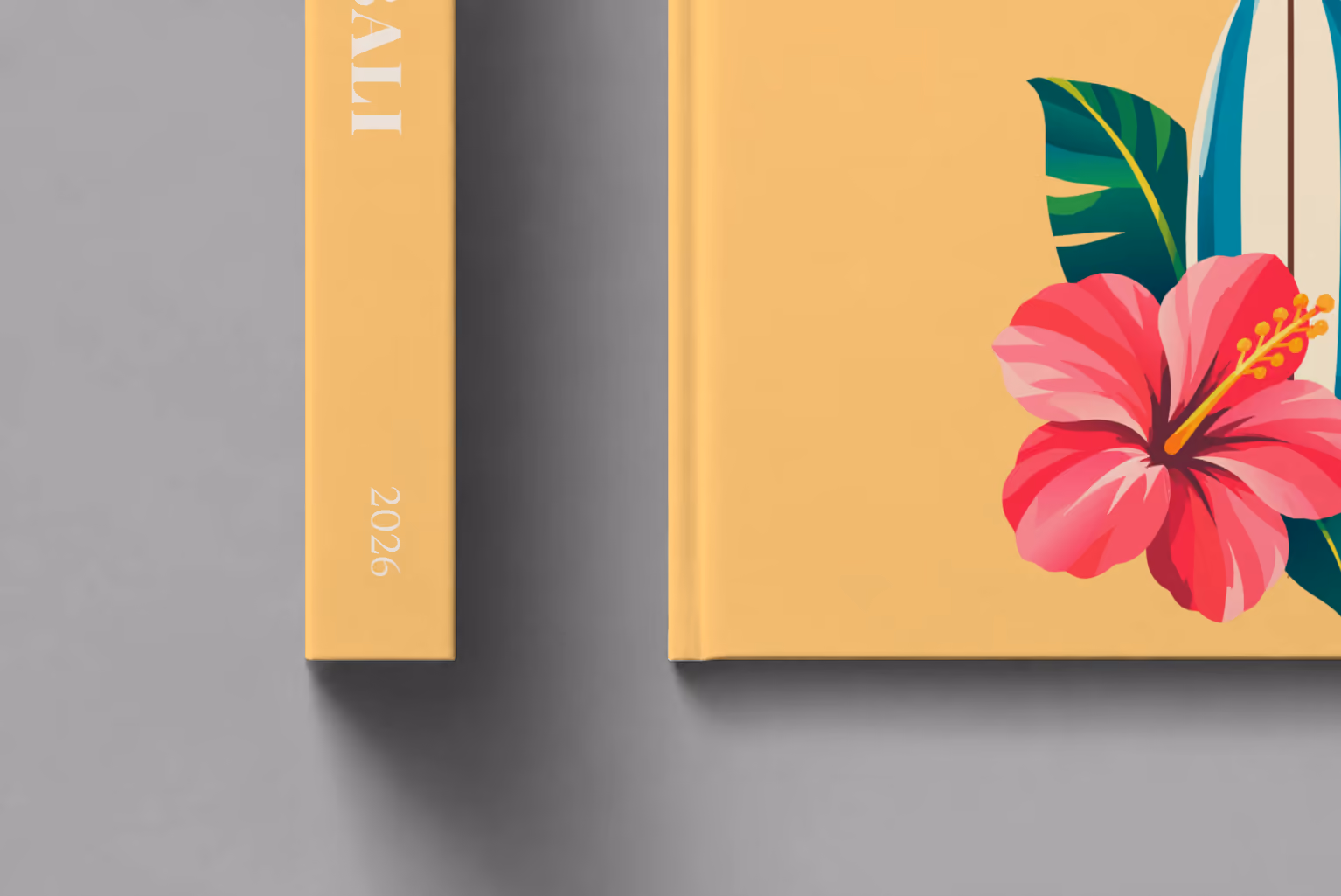 Bali hardcover photo book with the illustrated cover of a surfboard with a pink hibiscus and palm leaves on apricot, shown close up beside its spine on a pale grey studio surface
