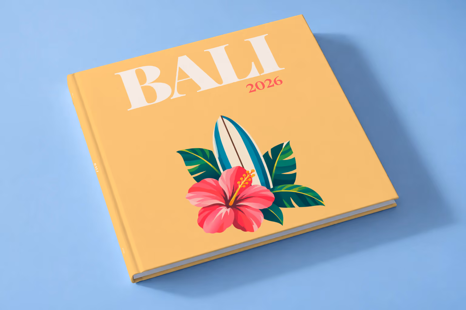 Bali square hardcover photo book with the illustrated cover of a surfboard with a pink hibiscus and palm leaves on apricot, lying on a pale blue studio backdrop