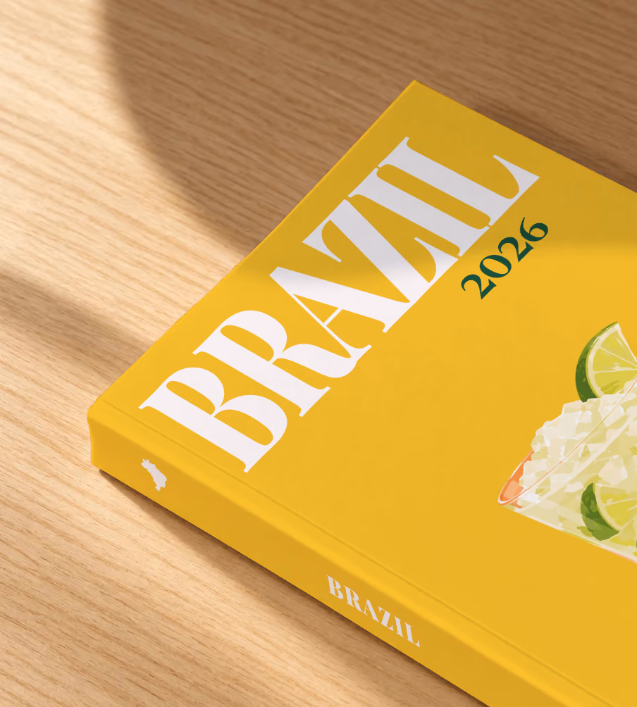 Brazil softcover photo book with the illustrated cover of a caipirinha with crushed ice and lime on golden yellow, lying on an oak desk in dappled afternoon sunlight